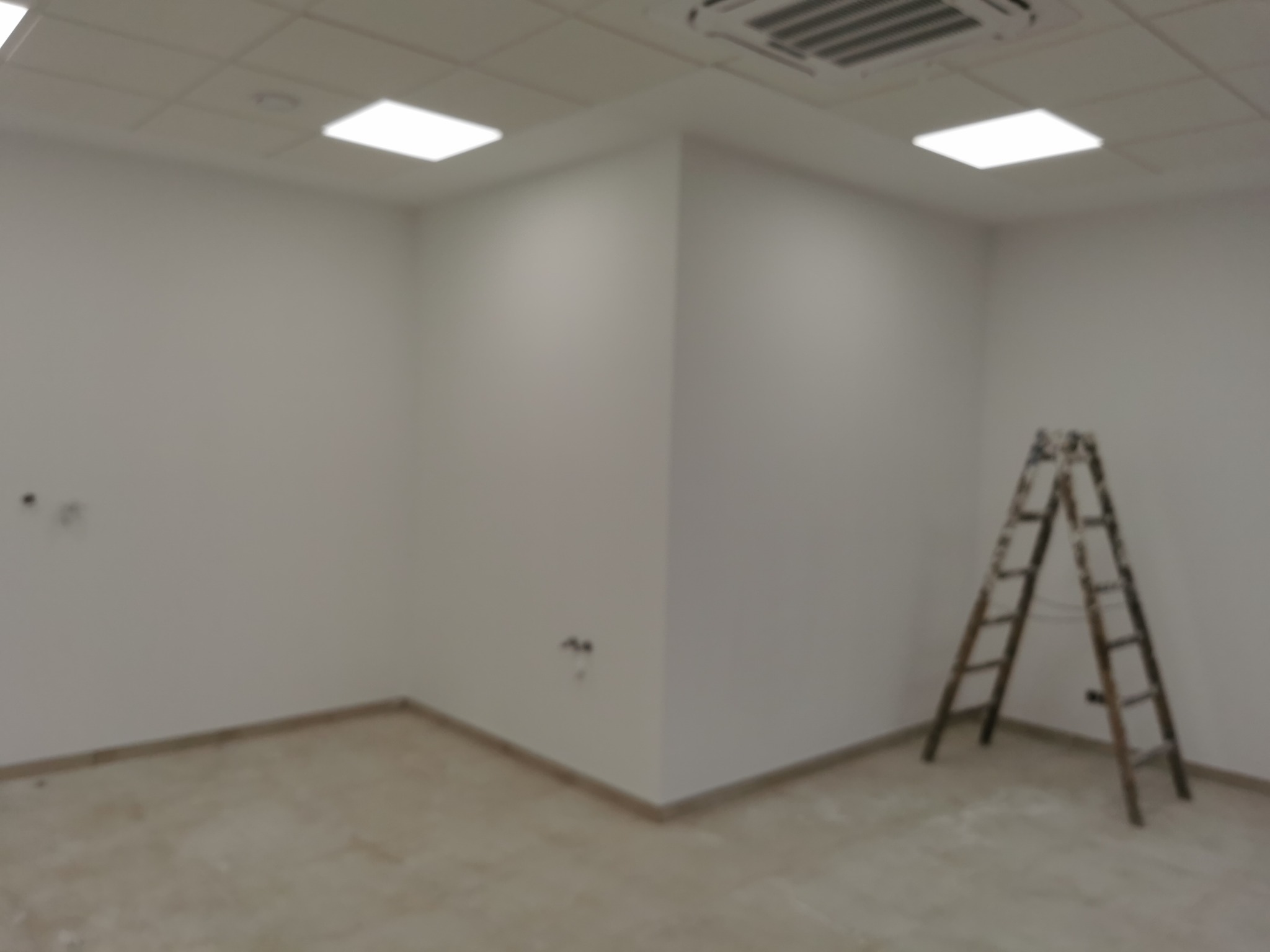 Pusta, jasna przestrzeń w Markach przygotowywana do remontu, z widoczną drabiną opartą o ścianę i widocznymi gniazdkami elektrycznymi.