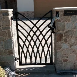 Czarna, metalowa furtka o dekoracyjnym wzorze, zamontowana między kamiennymi słupkami z adresem Żytnia 3a, widoczny kabel wystający ze słupka.