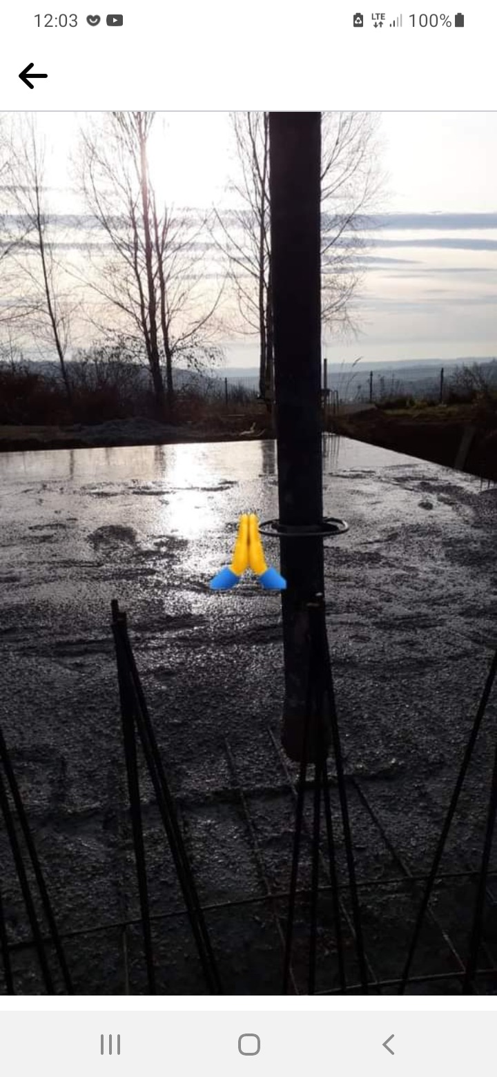 Fundament pod dom w trakcie wylewania betonu, widoczna stalowa siatka zbrojeniowa i rura do pompowania betonu, w tle krajobraz.