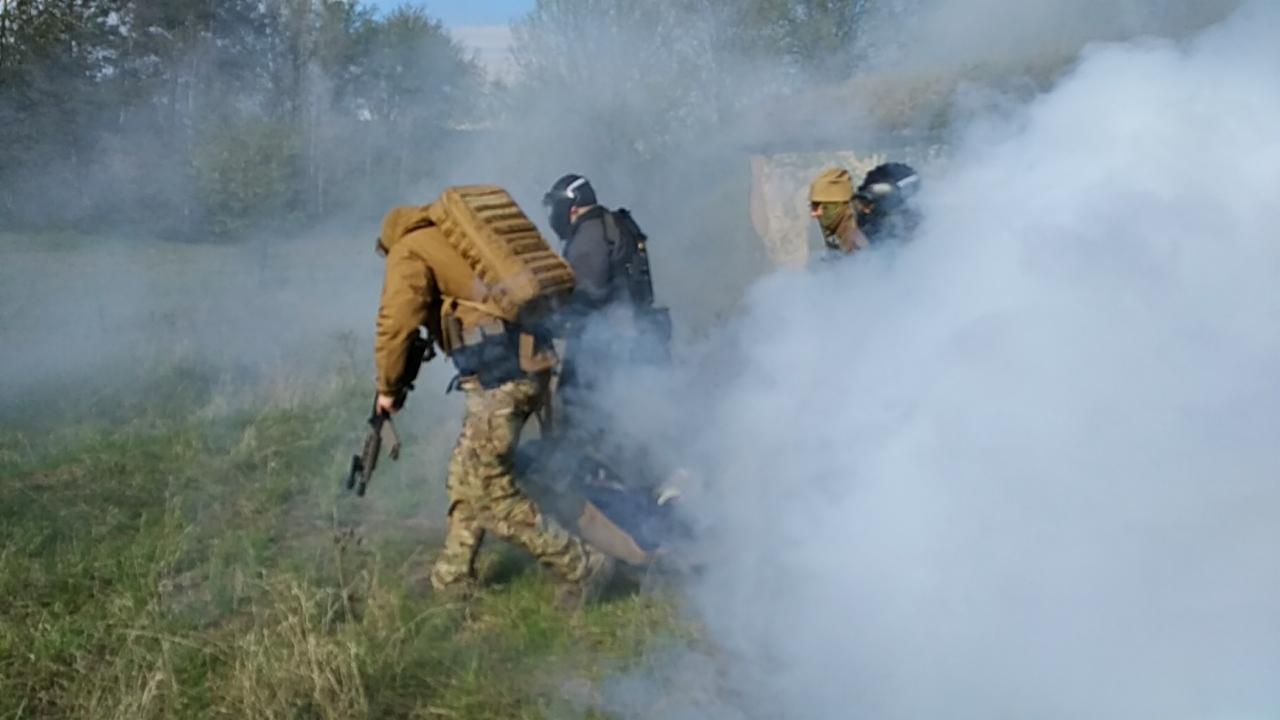 Symulacja akcji ratunkowej z użyciem dymu: ratownicy w strojach taktycznych ewakuują poszkodowanego na noszach polowych.