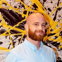 Portret mężczyzny z rudą brodą na tle abstrakcyjnego obrazu z czarnymi i żółtymi plamami.