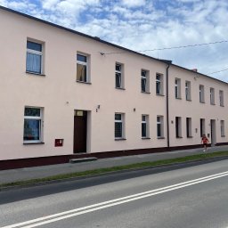 Usługi Ogólnobudowlane Bartosz Rospłoch - Długi budynek mieszkalny z jasnoróżową elewacją i białymi oknami, widoczny z poziomu ulicy w słoneczny dzień z lekkim zachmurzeniem.