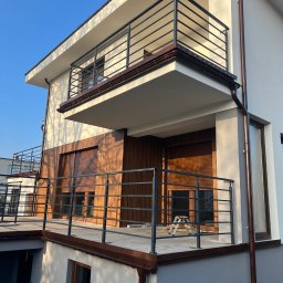 Usługi Ogólnobudowlane Bartosz Rospłoch - Nowoczesny dom z balkonami i drewnianą elewacją, oświetlony popołudniowym słońcem. Widoczne detale wykończenia i elementy architektoniczne.