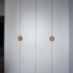 M&R MEBLE - Biała szafa wnękowa z czterema drzwiami i okrągłymi, drewnianymi uchwytami, na drewnianej podłodze.