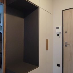 M&R MEBLE - Biało-szara szafa w przedpokoju z wnęką i otworem na legowisko dla zwierząt, minimalistyczne drewniane uchwyty, widok na drzwi wejściowe.