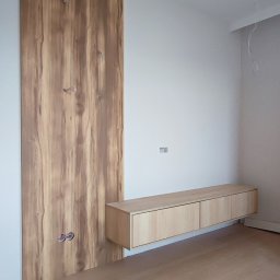 M&R MEBLE - Drewniana ściana z ukrytymi przewodami i wisząca szafka RTV w minimalistycznym wnętrzu z drewnianą podłogą.