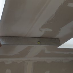 GRZEGORZ Zabagło - Sprawdzanie poziomu sufitu z płyt kartonowo-gipsowych przy użyciu poziomicy, widoczne łączenia płyt i okno dachowe.