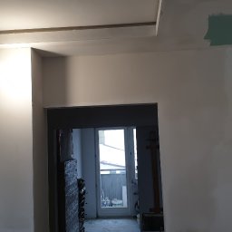 GRZEGORZ Zabagło - Wnętrze w trakcie remontu: gładzie na ścianach, fragment sufitu podwieszanego z płyt karton-gips, widoczne ślady szpachlowania i prowizoryczna lampa z drewnianą oprawką