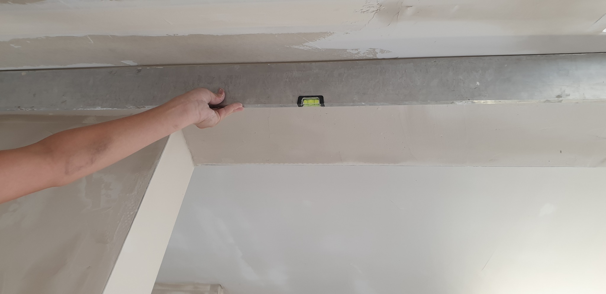 Sprawdzanie poziomu ściany przy użyciu poziomicy i metalowej listwy podczas szpachlowania sufitu.