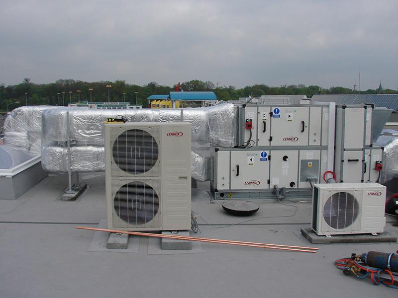 Instalacja klimatyzacji i wentylacji na dachu budynku z widocznymi jednostkami zewnętrznymi, izolowanymi przewodami i butlą gazową do lutowania.