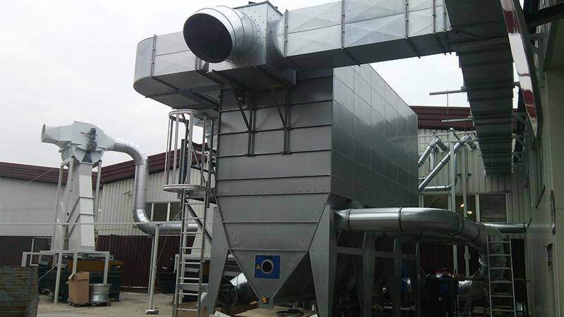 Duży, przemysłowy system wentylacji z metalowymi kanałami i drabinką, zainstalowany na zewnątrz budynku z widocznymi elementami konstrukcyjnymi.