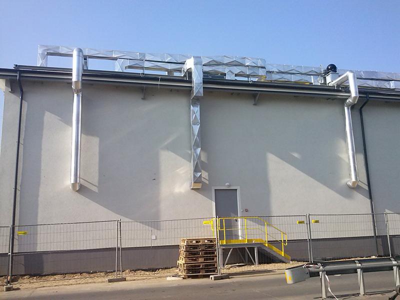 Zewnętrzny montaż systemu wentylacji z rurami spiro na elewacji budynku komercyjnego, widoczne elementy konstrukcyjne i zabezpieczenia budowy.