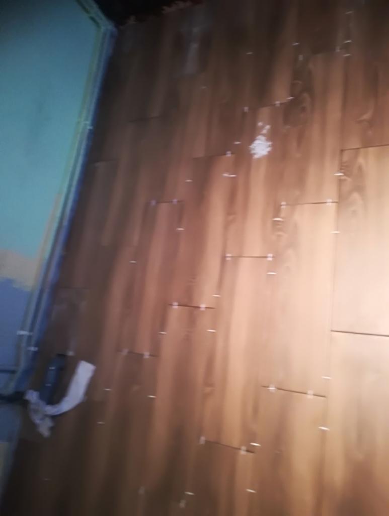 Ściana w trakcie wykańczania panelami ściennymi z widocznymi krzyżykami dystansowymi, fragment instalacji elektrycznej w tle.