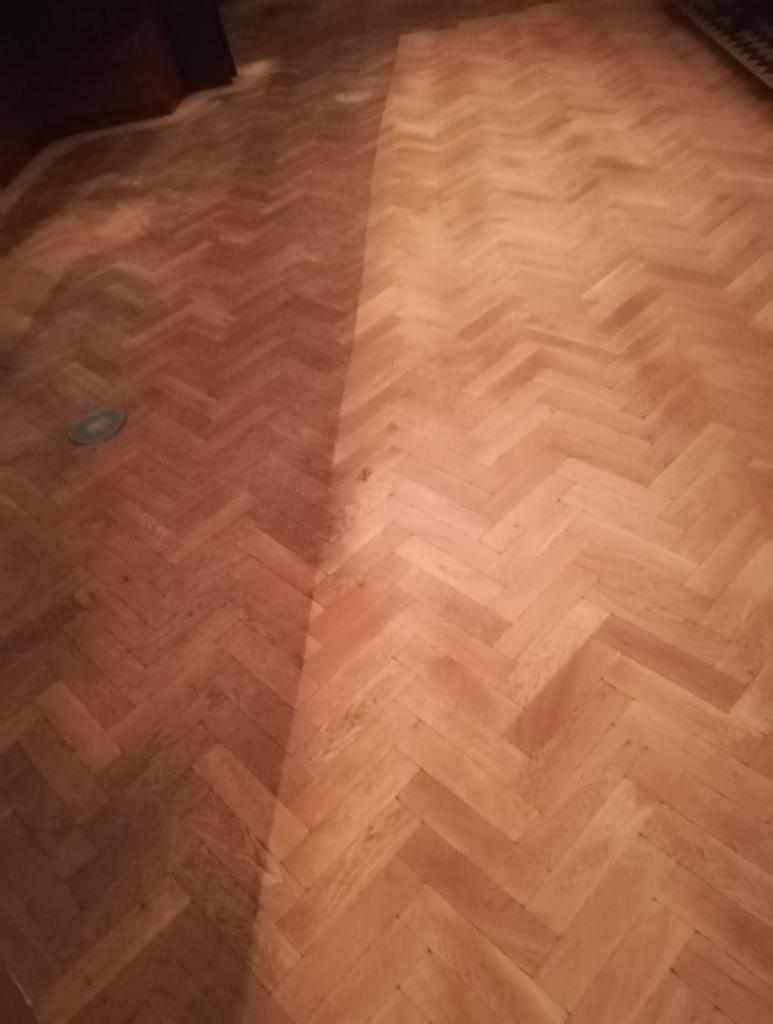 Parkiet ułożony w jodełkę, z widocznym kontrastem pomiędzy częścią odnowioną a tą przed renowacją, ukazujący różnicę w kolorze i połysku.