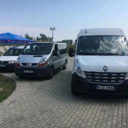 Flota trzech pojazdów: biały Volkswagen, srebrny Renault Trafic i biały Renault Master z symbolem osoby niepełnosprawnej, stojące na brukowanym podjeździe w słoneczny dzień.