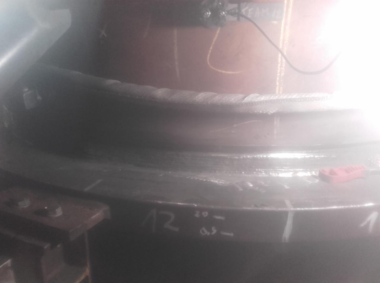 Spoina obwodowa na metalowej konstrukcji, widoczne ślady po spawaniu, oznaczenia numeryczne na powierzchni.