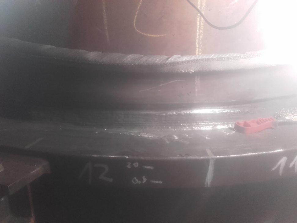 Spoina na grubościennej rurze stalowej z oznaczeniami pomiarowymi wykonanymi kredą, widoczny zacisk spawalniczy i kabel zasilający.