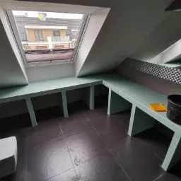 Montaż płyt karton gips w łazience na poddaszu we Wrocławiu, widoczne stelaże pod zabudowę umywalki i toalety, czarne płytki na podłodze, okno dachowe.