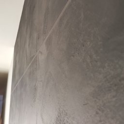 Wróbel Build Group - Szara ściana z efektem betonu architektonicznego, widoczna z bliska pod kątem, z delikatnymi przetarciami i pionowymi liniami podziału.