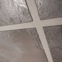 Wróbel Build Group - Szare płytki imitujące kamień z jasną fugą krzyżową, zbliżenie na powierzchnię z widoczną strukturą i detalami.