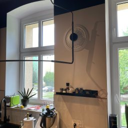 Wróbel Build Group - Nowoczesna kuchnia po remoncie: białe płytki, czarny blat, dekoracyjny plafon, okno z widokiem na zieleń, widoczny sprzęt AGD i dekoracje.