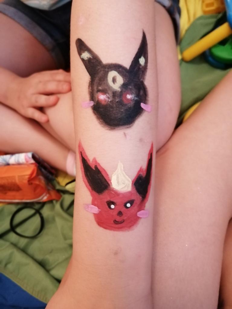 Dwa ręcznie malowane, kolorowe wizerunki postaci z bajek na nodze dziecka, z widocznymi pociągnięciami pędzla i niedoskonałościami, ukazujące amatorski charakter wykonania.