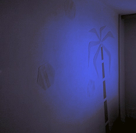 Dekoracyjna ściana z geometrycznymi wzorami i motywem palmy, oświetlona niebieskim światłem, tworząca unikalny efekt wizualny we wnętrzu.