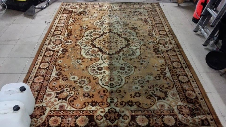 Duży, brązowo-beżowy dywan z kwiatowym wzorem, widoczne dwa białe pojemniki i sprzęt do czyszczenia dywanów w tle.