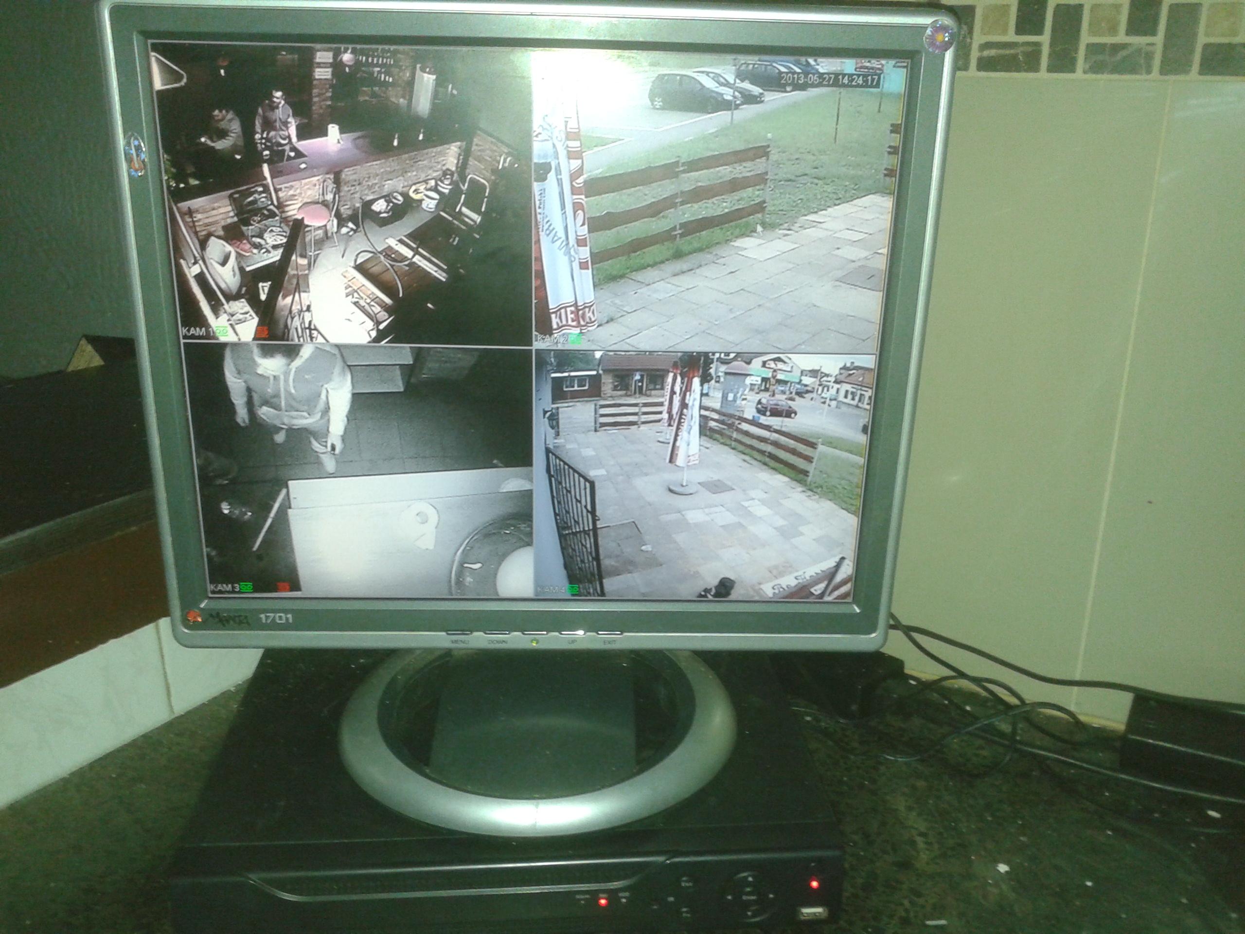 Monitor CCTV wyświetlający obraz z czterech kamer: wnętrze baru, parking, wejście do budynku i widok z góry na osobę. Nagranie datowane na 27 maja 2013.