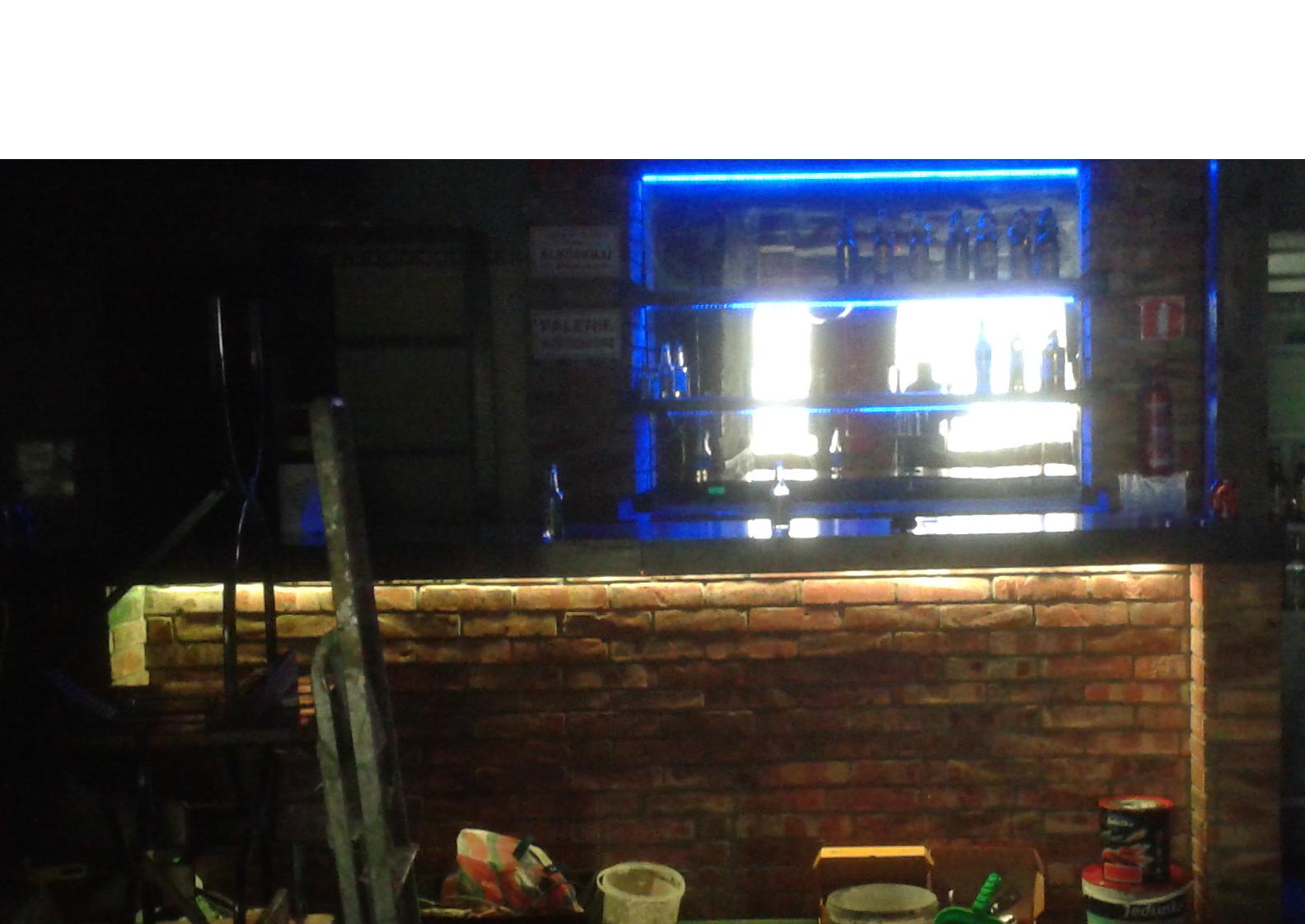 Bar z ceglanym frontem, podświetlony taśmą LED, w trakcie prac wykończeniowych, widoczne narzędzia malarskie i drabina.