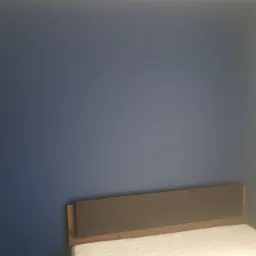 Sypialnia po malowaniu ścian na granatowo, widoczny fragment łóżka z szarym zagłówkiem i biały fragment ściany obok