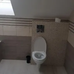 Ukończona łazienka na poddaszu ze skośnym sufitem, z wanną, toaletą i wykończoną glazurą w odcieniach beżu i szarości, widoczne niedociągnięcia w postaci braku listwy przy podłodze.