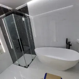 Nowoczesna łazienka z czarno-białymi marmurkowymi płytkami, kabiną prysznicową typu walk-in z czarnymi profilami i wolnostojącą białą wanną owalną, oświetlenie LED w suficie.