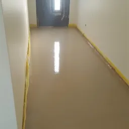 Świeżo wylana, mokra posadzka jastrychowa z widocznym odblaskiem światła z okna, zabezpieczona żółtą taśmą malarską przy ścianach.