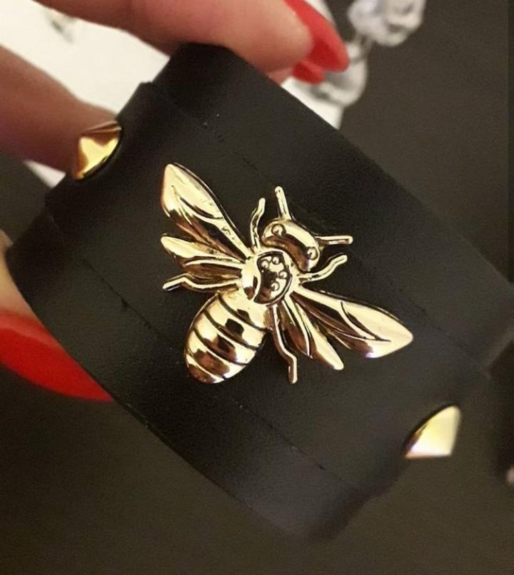 Czarna, skórzana bransoletka z metalową aplikacją w kształcie złotej pszczoły i ozdobnymi nitami.