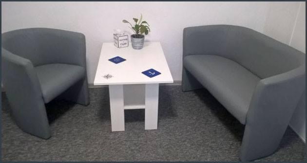 Pokój z szarym fotelem, kanapą i białym stolikiem z dekoracjami w postaci naklejek i rośliny doniczkowej