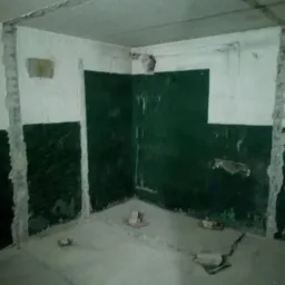 Wnętrze pokoju w trakcie prac remontowych: częściowo usunięte tynki, odsłonięte cegły, zielona farba na ścianach, gruz na podłodze.