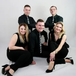 Zespół muzyczny w czarnych strojach z krawatami w klawisze fortepianu pozuje na białym tle.