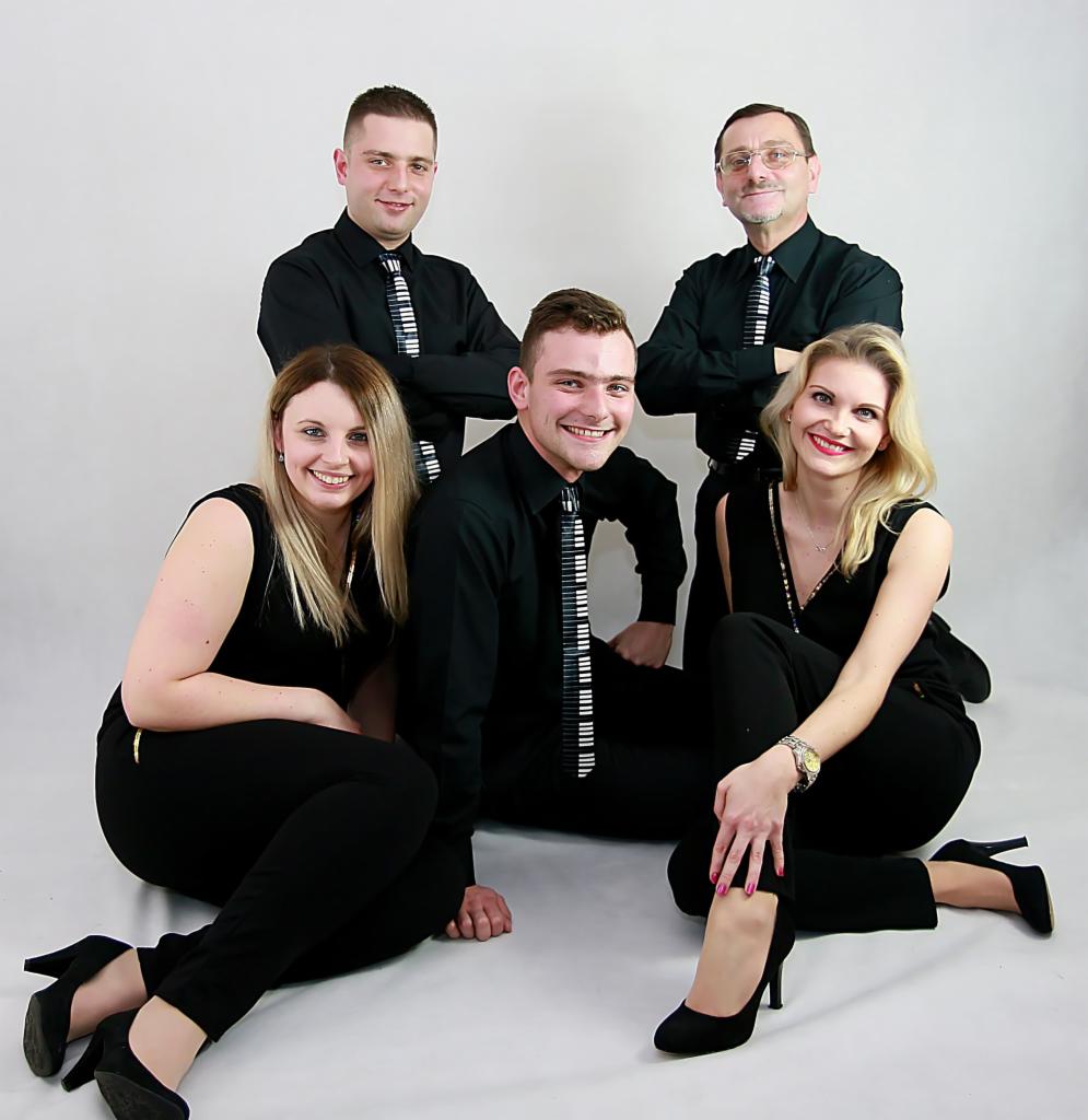 Zespół muzyczny w czarnych strojach z krawatami w klawisze fortepianu pozuje na białym tle.