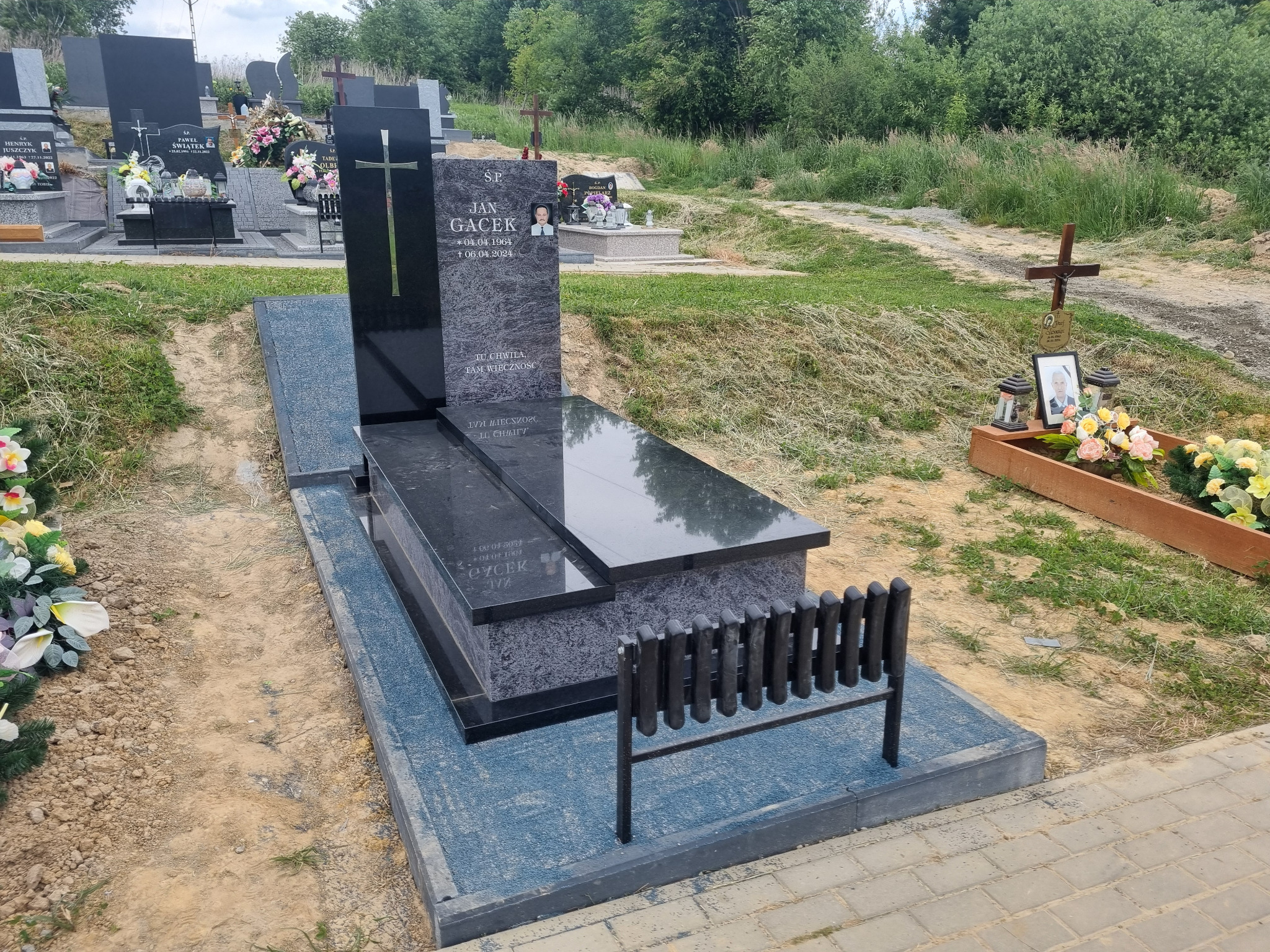 Nowoczesny nagrobek z ciemnego granitu Orion i Bengal Black z wysoką tablicą, prosta forma, otoczenie cmentarne.