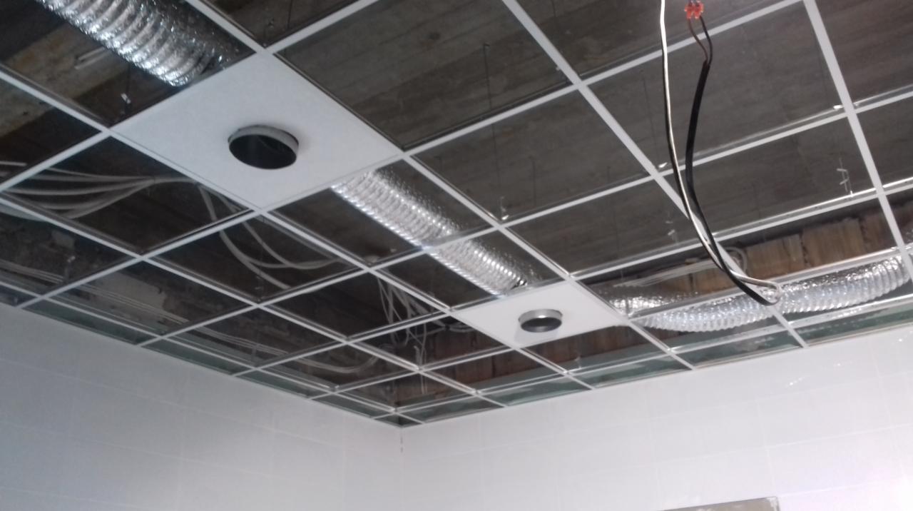 Sufit podwieszany w biurze z widocznymi elementami instalacji: rurami wentylacyjnymi, przewodami elektrycznymi i otworami na oświetlenie.