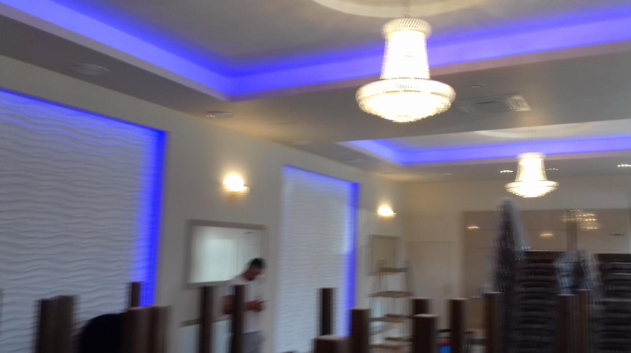 Jasne wnętrze biurowe z dekoracyjną ścianą 3D, oświetleniem LED i kryształowymi żyrandolami, przygotowywane do użytku, z widocznymi elementami wyposażenia i osobą w tle.