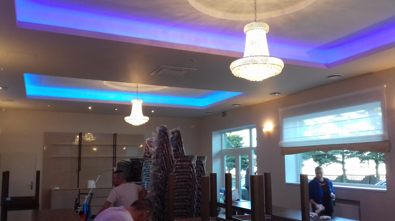 Jasne wnętrze biura z niebieskim oświetleniem sufitowym, żyrandolami i stosem krzeseł w folii ochronnej, przygotowywane do użytku.