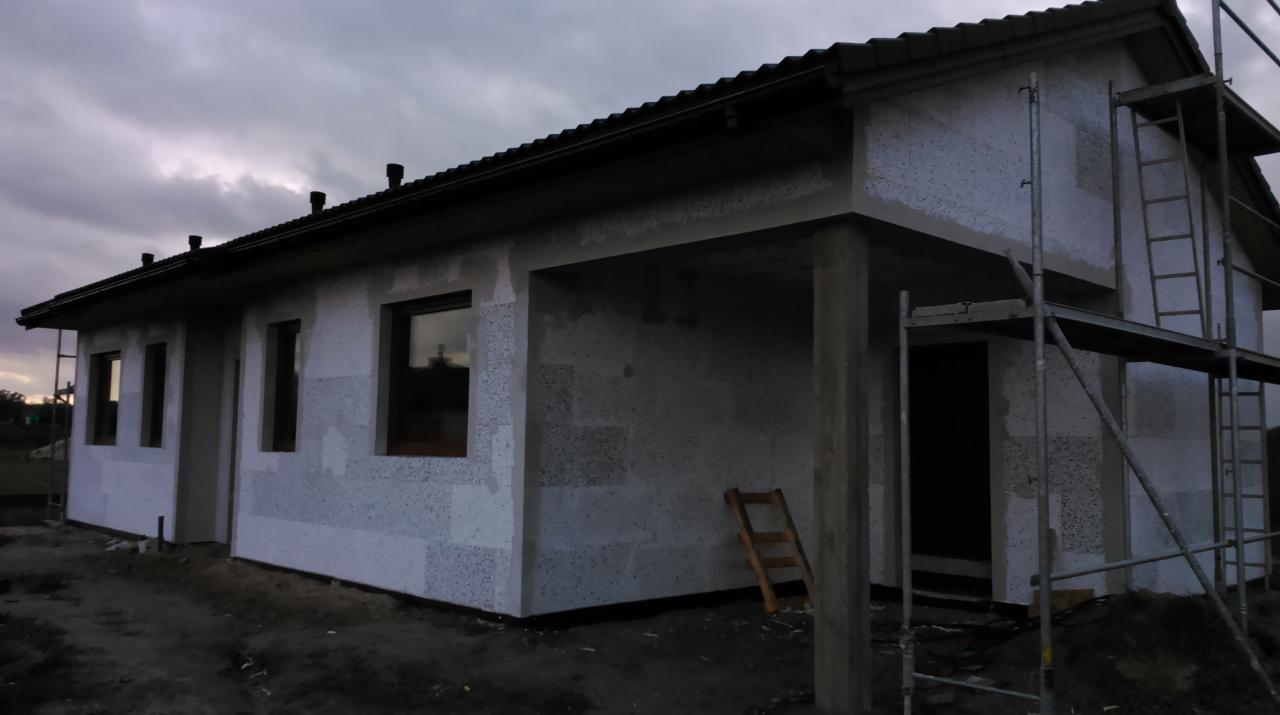 Dom jednorodzinny w trakcie ocieplania styropianem, widoczne rusztowania i drabina, pochmurne niebo.