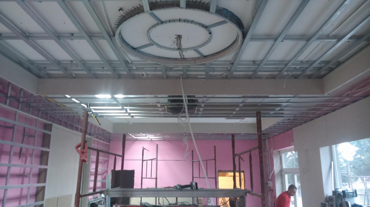 Montaż sufitu podwieszanego z metalową konstrukcją i okrągłym elementem dekoracyjnym na tle różowych ścian w trakcie remontu.