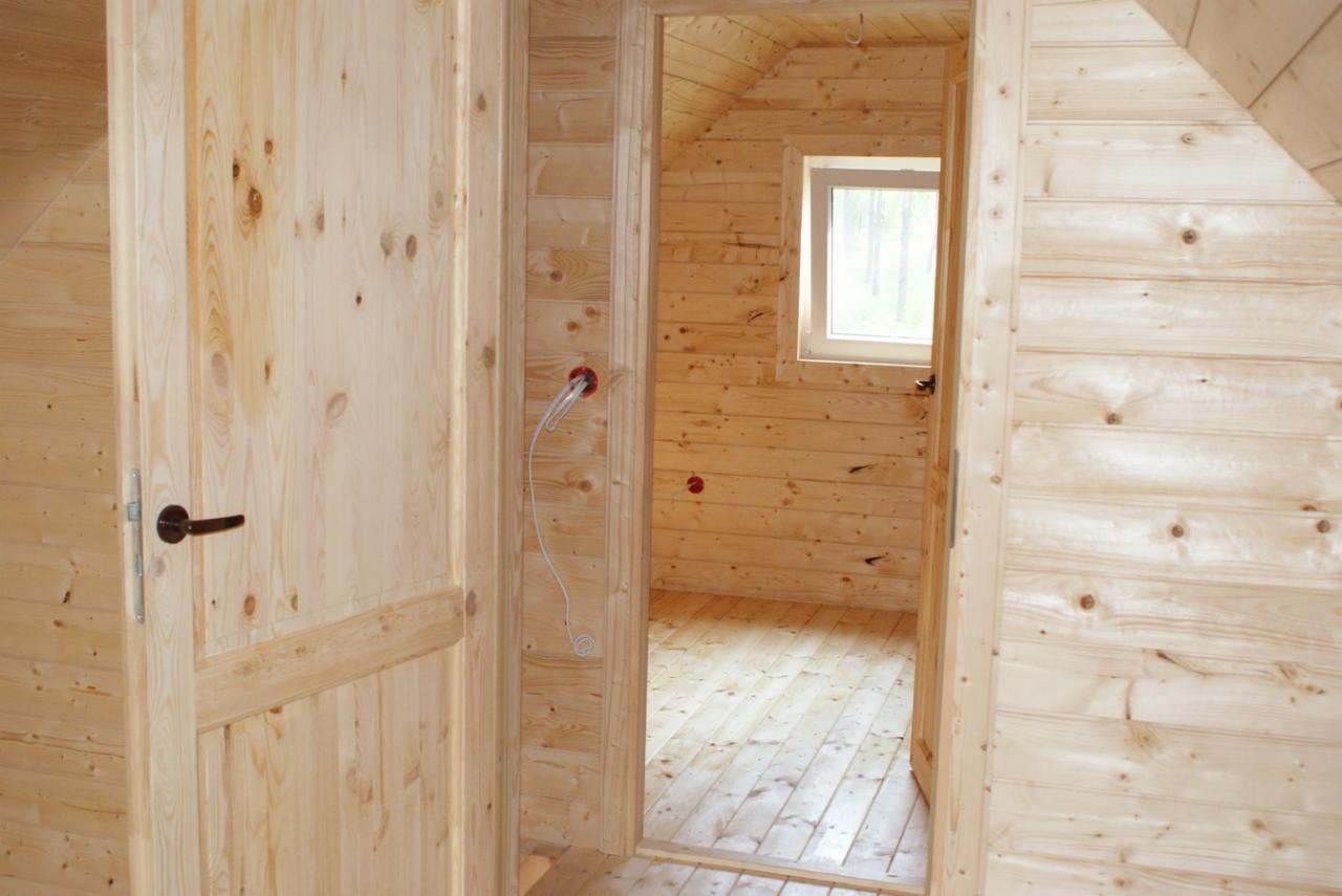 Wnętrze domku drewnianego o powierzchni 70 m2, wykończonego jasnym drewnem, widok z korytarza na pokój z oknem, widoczne instalacje elektryczne w ścianie.