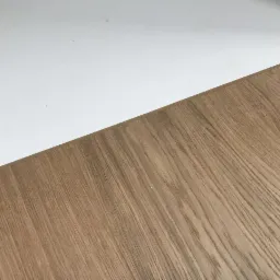 Fragment podłogi z jasnego drewna sąsiadujący z białą powierzchnią, ujęcie z góry, widoczne naturalne usłojenie drewna.