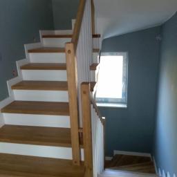 Usługi Parkieciarskie - Drewniane schody z białymi podstopnicami i drewnianą balustradą, oświetlone przez okno, prowadzące na dół.
