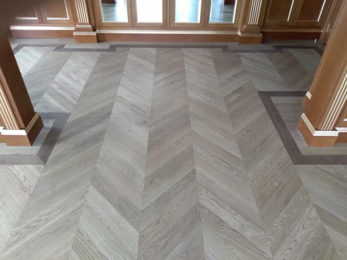 Jasnoszara podłoga ułożona w jodełkę francuską, obramowana ciemniejszą listwą przy kolumnach i drzwiach.