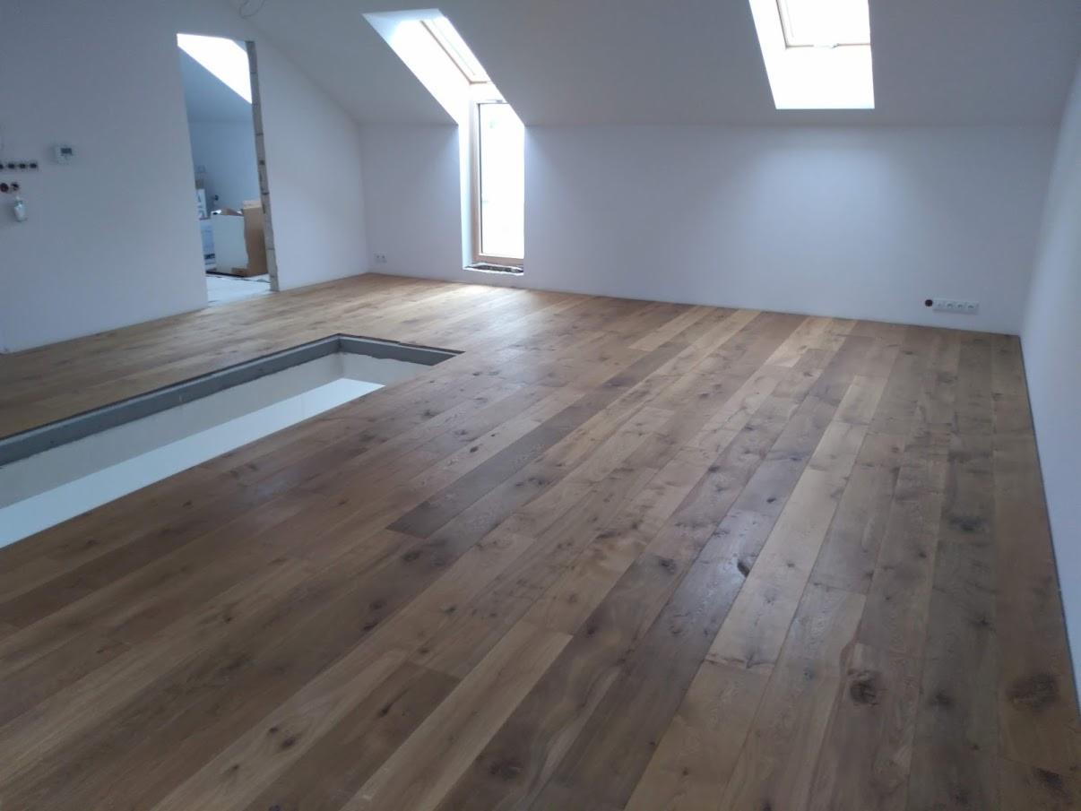 Ułożony parkiet w jasnym poddaszu z oknami dachowymi, widoczna wnęka w podłodze z przygotowaną przestrzenią na schody.